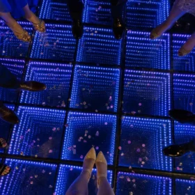 Overhead view of an infinity mirror LED dance floor glowing blue and purple at a birthday party