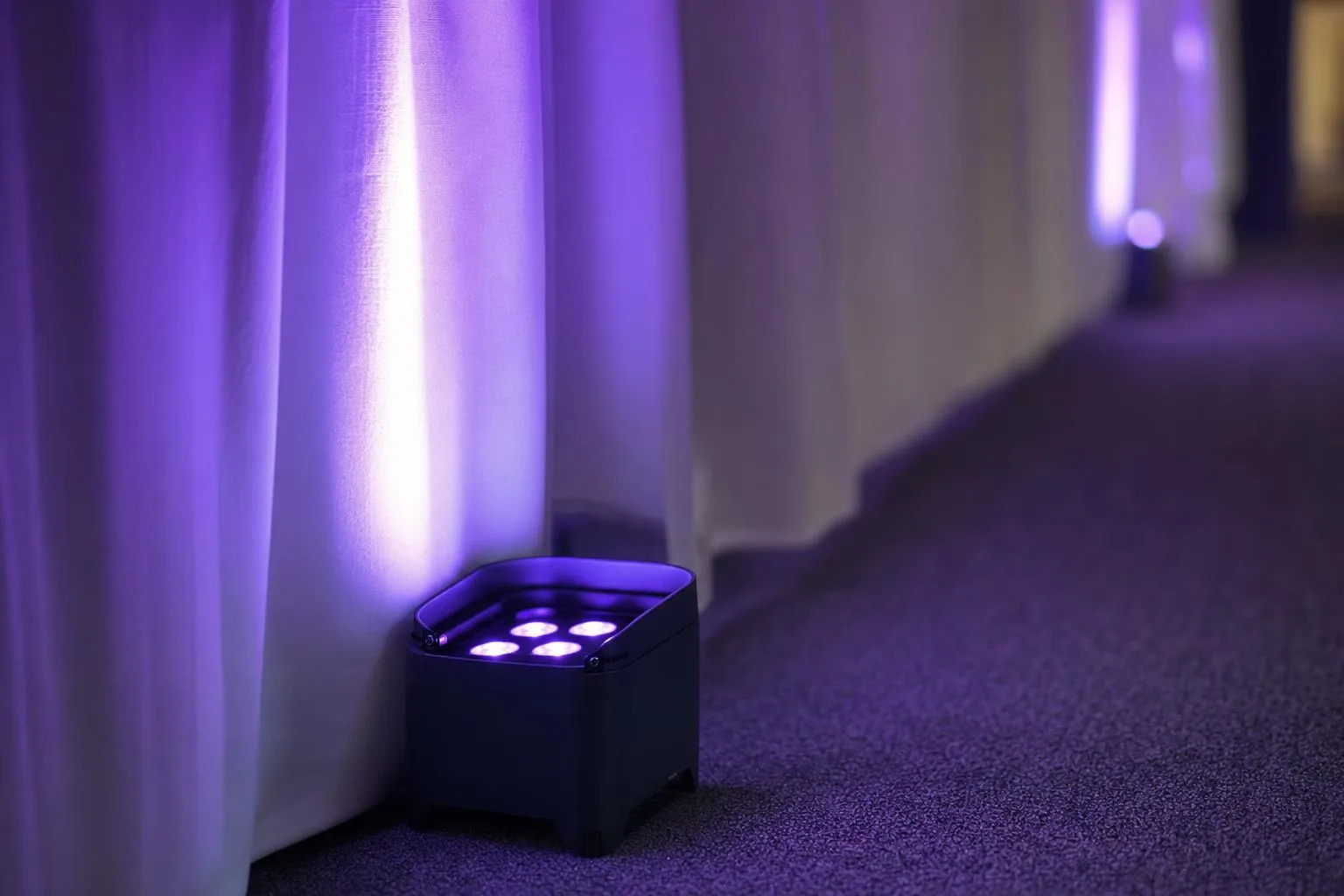 Battery powered wireless LED uplight washing a white drape in purple